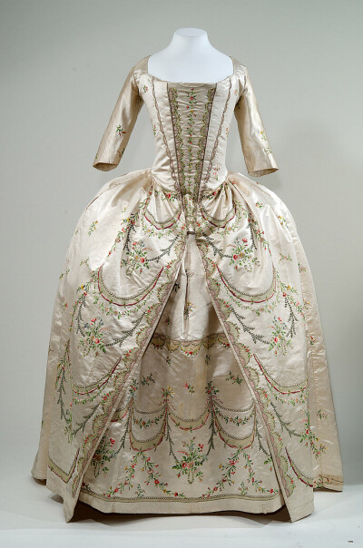一件1780年代英式女袍，在白色缎子上用彩线绣出纤细的花枝，让人有种春天的清风吹拂而来的感觉。 ​​​