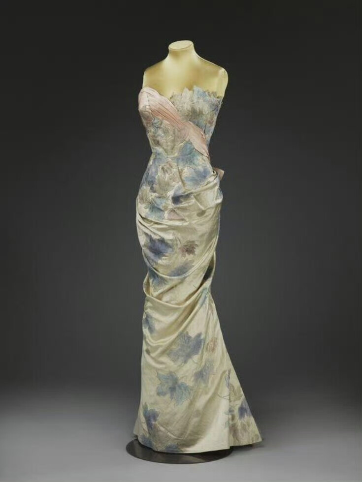 法国时装设计师皮埃尔·巴尔曼（Pierre Balmain，1914-1982）在1950年代左右设计的女士长裙。Balmain时装屋于1945 年开业，很快以其优雅的设计及精致的版型轮廓，俘获了包括温莎夫人等众多名媛的芳心。在他的设计中我们可以看到大裙摆、纤细腰身以及浪漫印花等50年代的代表性元素，他和迪奥先生都是战后复兴巴黎传统优雅的女装设计的先锋。