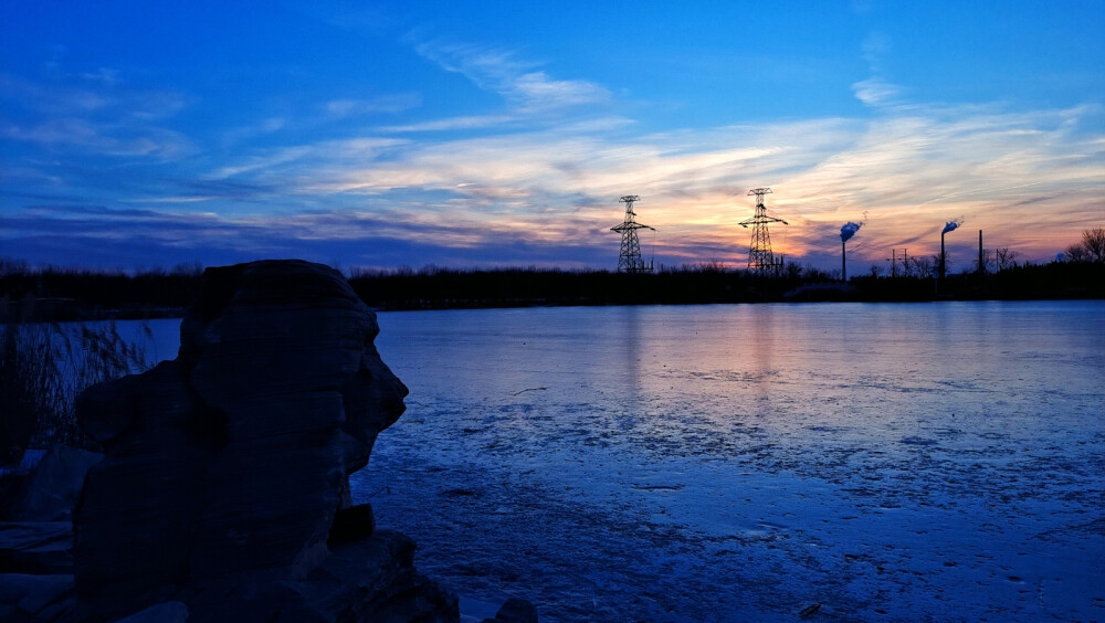 奇特岩石影像记忆。天空由青灰色逐渐呈现出醉人的蓝色，夕阳西下，落日余晖洒在冰面，如梦如幻。奇特的岩石和冰湖静静地守护着这片宁静。远处，两座铁塔默默地矗立，袅袅炊烟徐徐升起，仿佛在诉说着企业的故事。在湖边漫步，感受着大自然的气息。这里没有喧嚣，只有风的呢喃和冰湖的低语。这一刻，我仿佛融入了这片美景，成为了它的一部分。神奇的冰湖，释放着自然的魅力。这里不仅有美丽的风景，还有无尽的宁静和祥和。我愿意将这份美好分享给每一个热爱生活的人。让你们一同享受这份喜悦，美好是我们大家所期望的，只要追求就有希望，美好时光生活幸福将能实现。