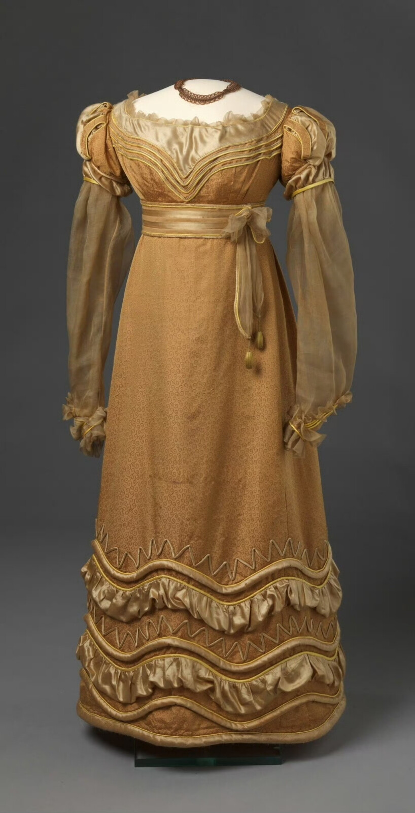 一件1825年的晚装，用金褐色漩涡花纹丝绸搭配暗金色与明黄色缎子制成，特别之处是在做成切口的泡泡袖下连着一条透明薄纱长袖，可以想象穿上身后面料质感的对比与双臂轻笼云雾中的效果。我在设计小玫瑰的衣服时就觉得这种样式的袖子应该存在于浪漫主义时期的服装中，果然这就找到了。