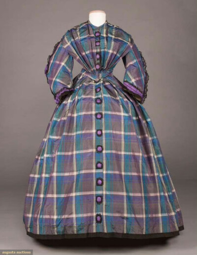 一件1859年的塔夫绸日装裙。虽然是很常见的格子花纹，但配色十分出彩，用各种青蓝紫交错，再搭配面料光泽，展现出仿佛肥皂泡表面的华丽幻彩效果。此外还有亮紫色丝绸和黑色蕾丝组合成的饰带与纽扣，就像为整件衣服又…