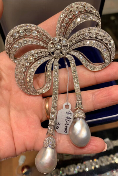 
这是爱德华时期(1900-1910年) 制作的古董铂金蝴蝶结胸针，镶嵌蕾丝花边的钻石，吊坠是两颗梨形的野生海水无核珍珠