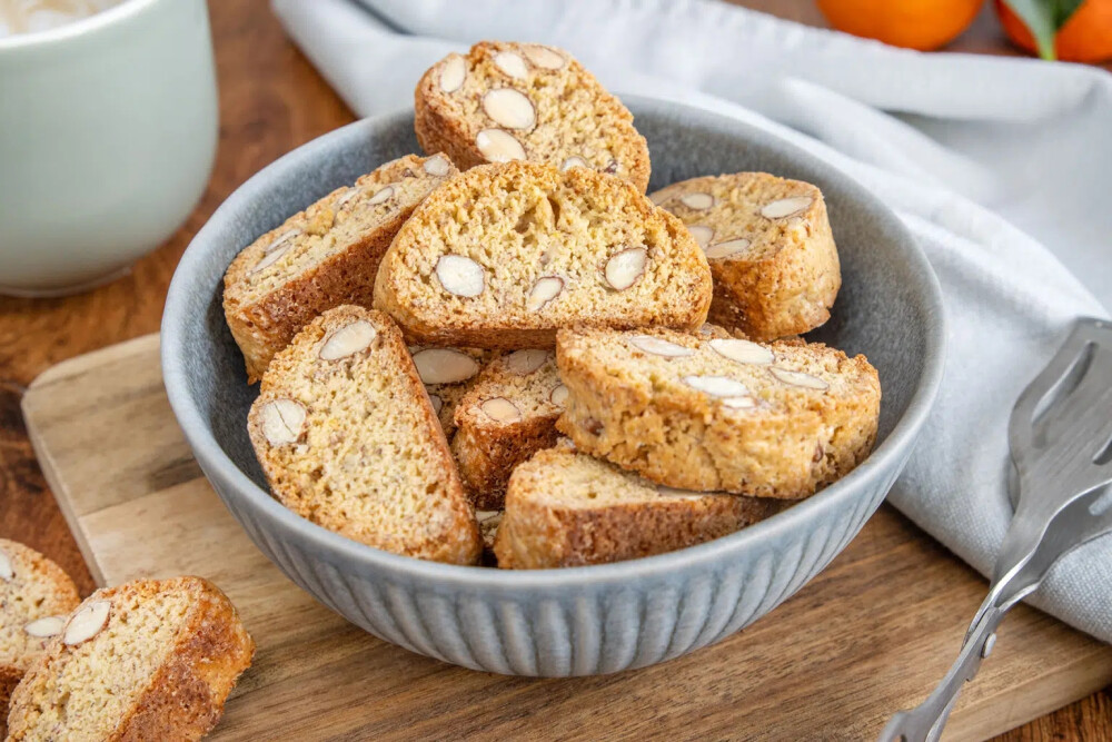 意大利甜品 Cantuccini 意式杏仁脆饼 诞生于中世纪托斯卡尼地区的传统点心，由各类干果或坚果制成的杏仁风味硬饼干，从里到外酥香爽脆。被咬断时还会发出细小的声响，因此命名时便参考了在意大利语中有着“微弱的歌声”这个意思的单=词“Cantocci/Cantucci”。由于太硬，意大利人常常把它浸在餐后葡萄酒(例如意大利甜白葡萄酒“Vin Santo”)或咖啡等饮料中，泡软之后再取出食用。添加了杏仁的意式长条饼干，是下午茶的极佳伴侣，蘸着咖啡或茶更是别有一番风味。加入杏仁也可以看做 Cantuccini Toscani O Biscotti di Prato