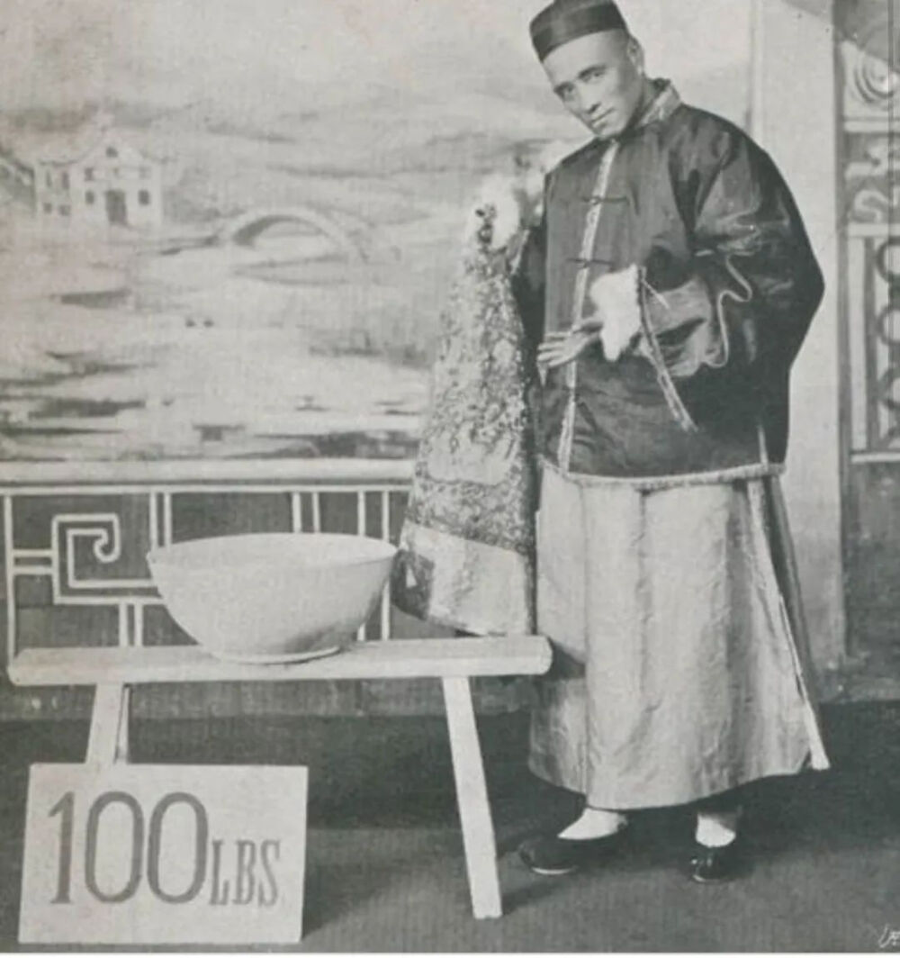 魔术师金陵福，本名朱连魁，1854年生于北京。照片为他在1898年赴美表演时的成名作，大碗飞水。照片中大碗下面的牌子上写着“100磅”，约45.4千克。当时他还用其他绝活征服了美国观众，比如从口中喷火或喷出浓烟，或者从口中取出一根大约4.6米长的杆子。他还有一项著名的魔术表演，金陵福在演出中突然用宝剑斩下助手男童的头颅，接着，无头的男孩转身并离开了舞台。