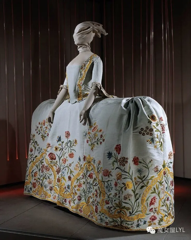 一件大画布。荷兰婚纱是刺绣的杰作。图案加上内敛的紧身胸衣和素色袖子，让人联想到一个服装花园的外观。17世纪的布料--丝带芥末卷轴、从胭脂红到腮红到蓝色的花朵，所有这些都以最浅的蓝色丝绸为背景，与18世纪的风格相匹配。