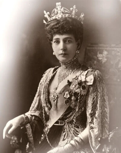 亚历山德拉王后委托卡地亚制作这条壮丽的钻石渔网项圈，镶嵌可拆卸的卡博雄祖母绿和红宝石。这些宝石取自印度土邦王赠予亚历山德拉王后的珠宝，后来玛丽王后也曾数次佩戴这件珠宝。