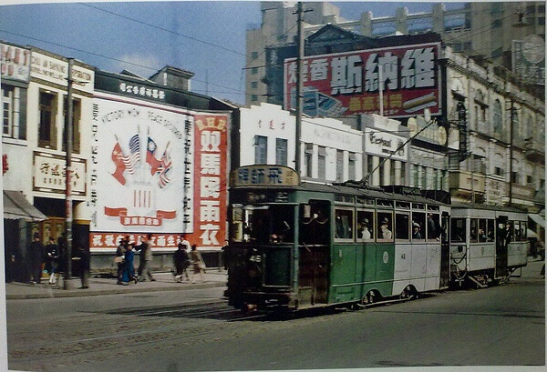 当当车。有轨电车在战时及战后的许多年里一直都行驶在南京东路上，其模样同美国、欧洲及印度的一些城市里的电车一样。街边那张巨型广告画，上面分别是中国、苏联、英国和美国的旗帜，以及“庆祝抗战胜利，庆祝世界和平”的标语。照片右上角的高大建筑是大新百货公司大楼（今第一百货大楼）。（艾伦•拉森 摄）