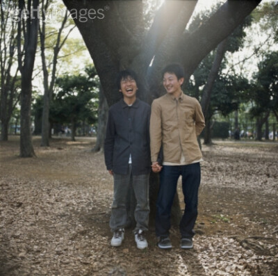 High-Res Stock Photography: Two men leaning against tree holding hands…