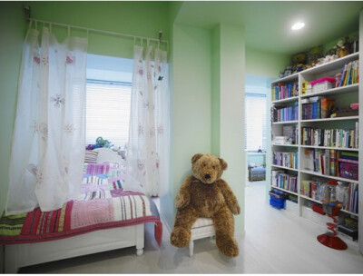房间承重支柱隐形的将房间分隔为两个区域。白色的地板搭配薄荷色的墙纸与天花板，让孩子觉得空间舒适无比。颜色绚烂的被子，让空间的色彩变得多元。白色的小矮凳，不仅便于孩子读书时的使用，平时把大型玩偶摆放在上…