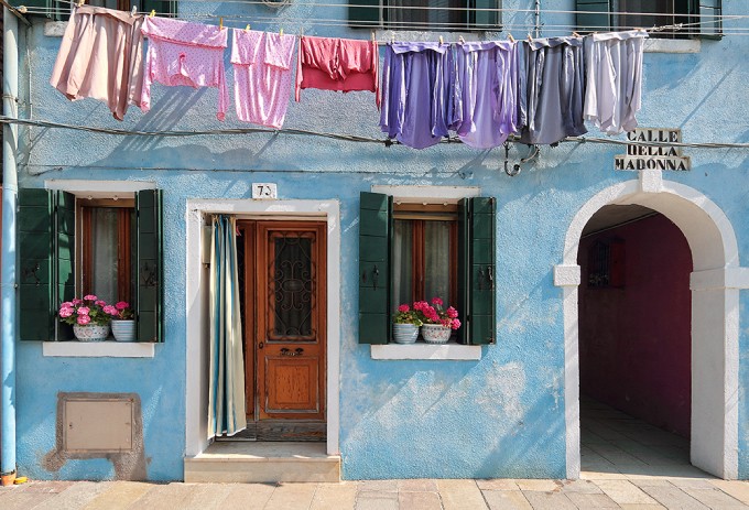 【Burano 布拉諾島】是義大利威尼斯潟湖上的島嶼，以手工蕾絲和彩色房子聞名於世。據說1481年達芬奇從希臘小城鎮Lefkara購回米蘭大教堂使用的壇布後，引進了花邊蕾絲，此技術於該島上生產製作，日後逐漸成為當地特產。彩色的房子其實最初是為了辨識家門的標示，居民確定顏色後必須向政府申請通過，才能彩繪，不同樣顏色的小房子並列，形成像童話故事裡才會有的彩色世界，相當可愛。by img splash