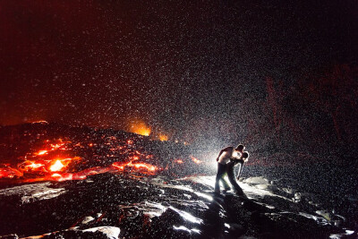 2012年度《国家地理旅行者》杂志摄影大赛的参赛作品之一，《Lava Kiss》，来自女摄影师Dallas Nagata White，画面中是她和她的丈夫，他们靠近夏威夷附近的一条活跃的熔岩流，架好三脚架拍下了这幅作品..