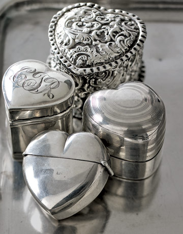 four silver heart shaped ring boxes on a silver platter