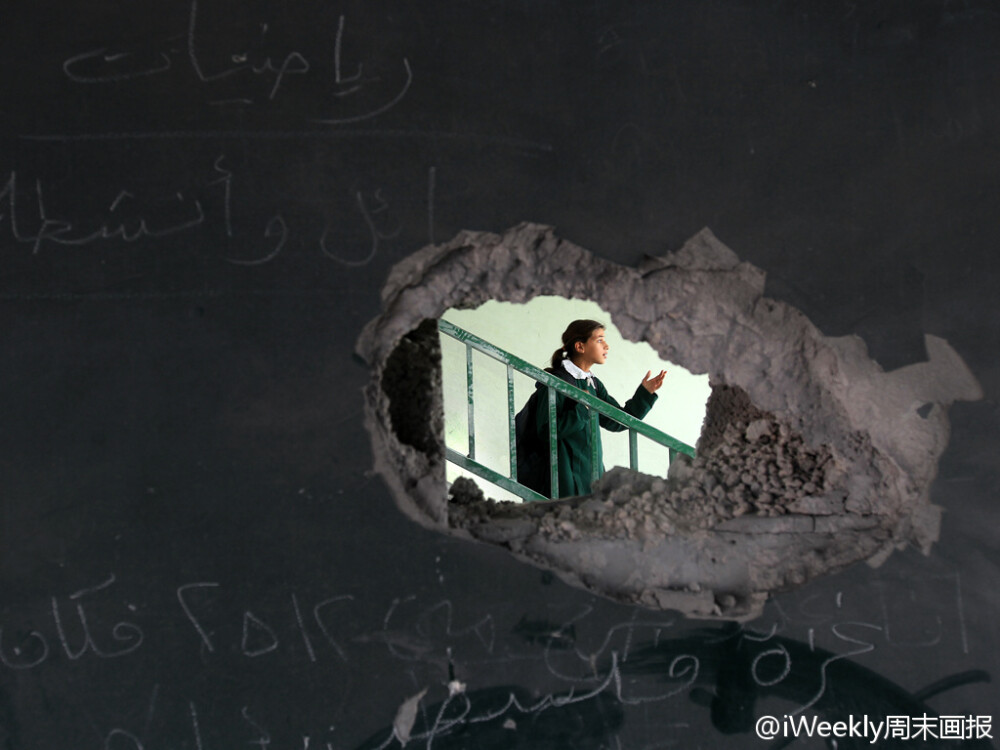 加沙地区，一位巴勒斯坦女孩站在一块在以色列空袭中被毁的黑板之后。摄影师：Mahmud Hams