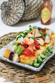 【海鲜金砖豆腐】做法： 1、准备好各类食材。 2、将青椒、香菇、草菇、番茄、洋葱洗净，切成大小均匀的丁状。鲜虾剥壳去虾线备用。 3、北豆腐一盒，取出后等分成5—6块，六面均匀的裹上淀粉。 4、平底锅加热，倒入食用油，将豆腐放入锅中中小火煎制。 5、及时翻面，待豆腐表皮呈金黄色有脆壳时取出放入盘中。 6、另起锅，倒入食用油，将葱花、红辣椒粒炒香。 7、放入洋葱、青椒大火翻炒。 8、再下入提前焯过水的香菇、草菇和虾仁翻炒，最后放入西红柿，加入盐、糖、少许黄酒。