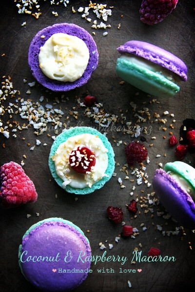 Teal and purple macaron cookies sandwich a white chocolate coconut infused ganache with a tart raspberry center and sprinkled with toasted coconut.