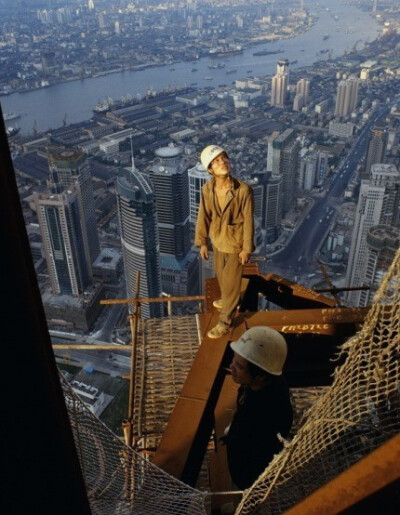 一名农民工身上沒有任何安全保护措施。百米高楼建筑工地上，夕阳的余辉洒在他身上，身后是上海陸家嘴CBD中心。