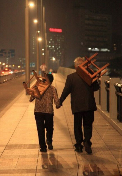 一对老人在宁波*看完“天然舞台”演出后，牵着手，扛着凳子从解放桥走回家。