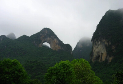  桂林月亮山风光图片。月亮山位于桂林阳朔县十里画廊景区末端，远远的你就可以看见山头上有一个天然的大石拱，两面贯通，酷似天上明月高挂，让你在一瞬间就被吸引！秀美古朴的月亮山是不是你想要一探究竟的旅游胜地…