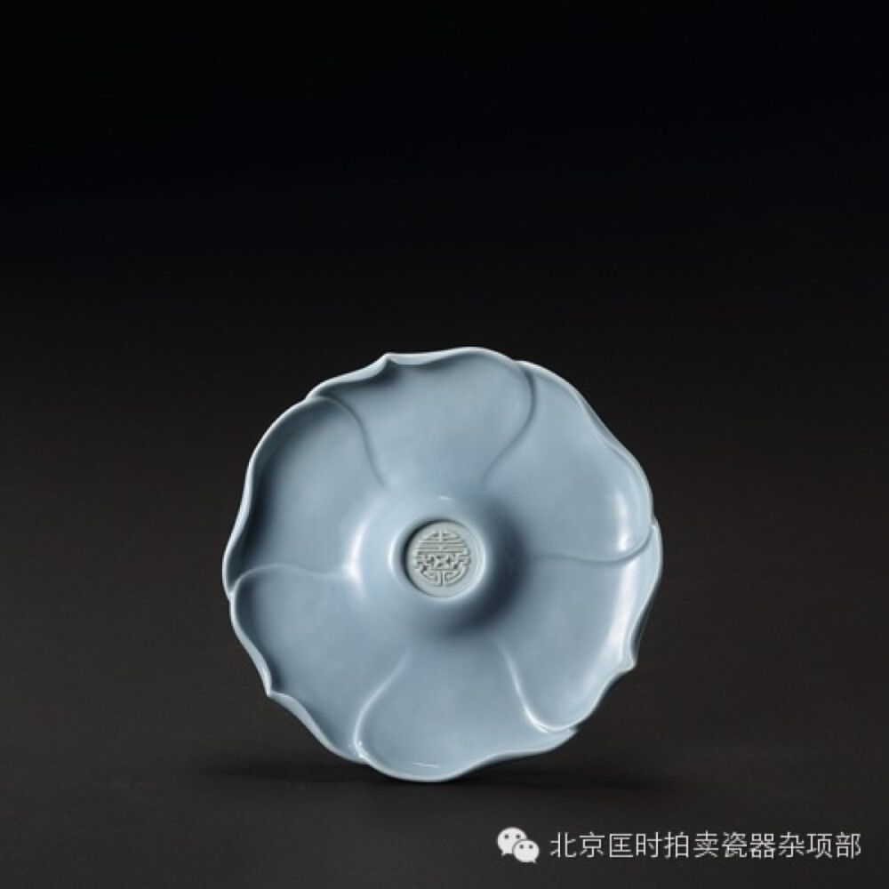 清雍正，天蓝釉团寿心葵花式盏托，L:13.8cm。盏托呈六瓣葵花形，花瓣相叠，底部均匀分布六枚支钉痕，圈足内凹，内书“雍正年制”四字篆书款。精致巧丽的造型惹人心扉。天蓝釉含氧化钴在1%以下的高温釉，康熙始烧，雍正更进一步。釉色淡雅悦目，可以与豇豆红媲美