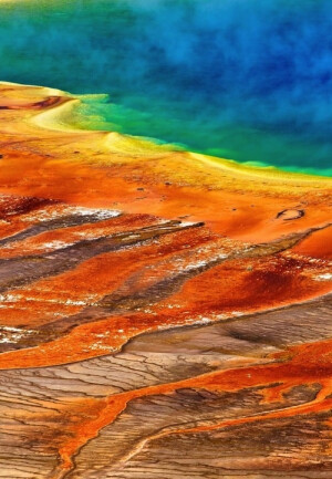 The Grand Prismatic Spring in Yellowstone National Park。美国黄石公园大棱镜温泉，又称大虹彩温泉。是美国最大，世界第三大的温泉。大稜镜温泉的美在于湖面的颜色随季节而改变，春季，湖面从绿色变为灿烂的橙红色，这是由于富含矿物质的水体中生活着的藻类和含色素的细菌等微生物，它们体内的叶绿素和类胡萝卜素的比例会随季节变换而改变，于是水体也就呈现出不同的色彩。