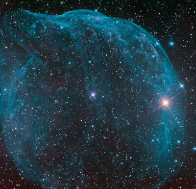  星云Sharpless308，这个巨大的宇宙泡泡云，是由一个炽热大质量恒星的高速恒星风所吹出来的。它位于大犬座内，而位于星云中心附近的蓝白色大质量恒星的恒星风扫起了先前演化阶段所抛出的较慢移动的物质，形成了这个…