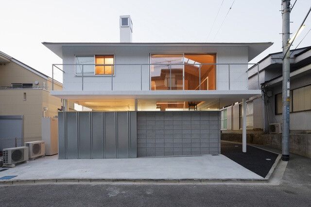 这座四坡屋顶的住宅位于日本兵库县川西市，由Tato Architects工作室设计。两层的住宅有着典型的澳大利亚“昆士兰风格”（The Queenslander）的大阳台。由于用地的局限，建筑一侧的公共道路非常狭窄，以至于建筑不得不将首层这一侧架空用以满足道路的通过宽度。首层包含了起居室、卫生间、储藏间、厨房餐厅以及车库等内容。以空心砖及玻璃材料进行围护。其中的的储藏间是由空心砌块围合而成的实体，在其上方设计师巧妙地设计了一个夹层空间，作为二层的工作间，利用高度的差异，工作间的桌面其实是二层的地板，而工作间的地板反而是储藏间的屋顶。 B162