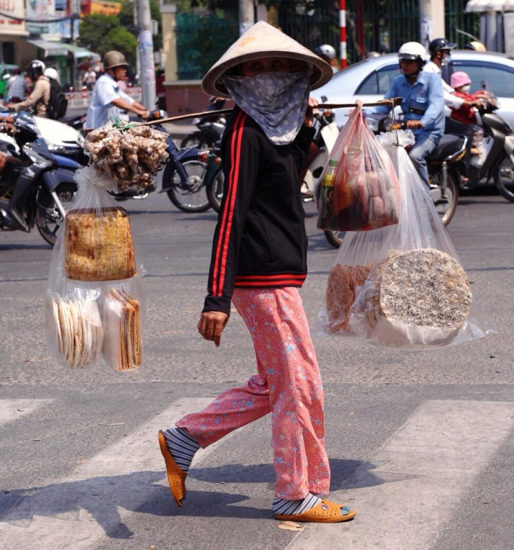 ◆越南，一名沿途叫卖的小贩，正穿过胡志明市的一条街道。