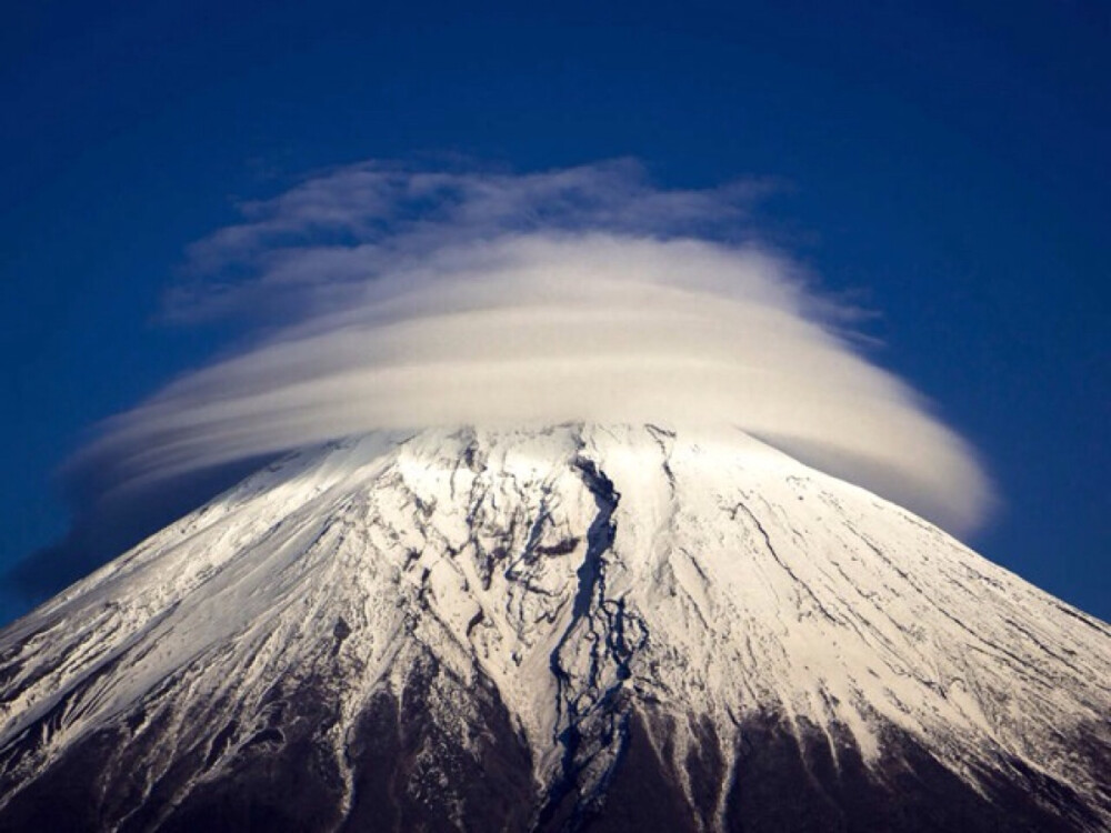  日本，富士山山顶被造型奇特的环状云笼罩。当潮湿空气在高纬度遇到楼房或山脉等阻碍物，背风面会生成驻波，同时空气中的水分逐渐凝结，便形成了类似的云。摄影师：Akihiro Shibata