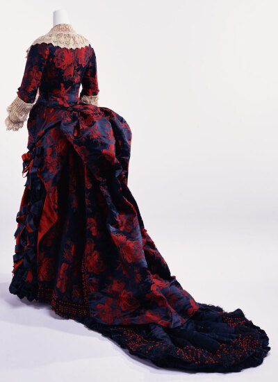 Dinner Dress，N.罗德里格斯 19 世纪 70 年代 深蓝色绿色和红色是绝佳的补色。创建时，其使用的是最新时尚的化学染料。织物在与黑暗和庄严的背景下，大而明亮的红色玫瑰图案能显示出颜色的新味道。像这种织物，刚度…