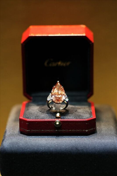 Cartier23.48克拉梨形切割深粉色偏橙色钻石戒指价值逾百万，在两枚闪耀钻石的鼎衬下，熠熠生辉的深粉色偏橙色钻石令人叹为观止。