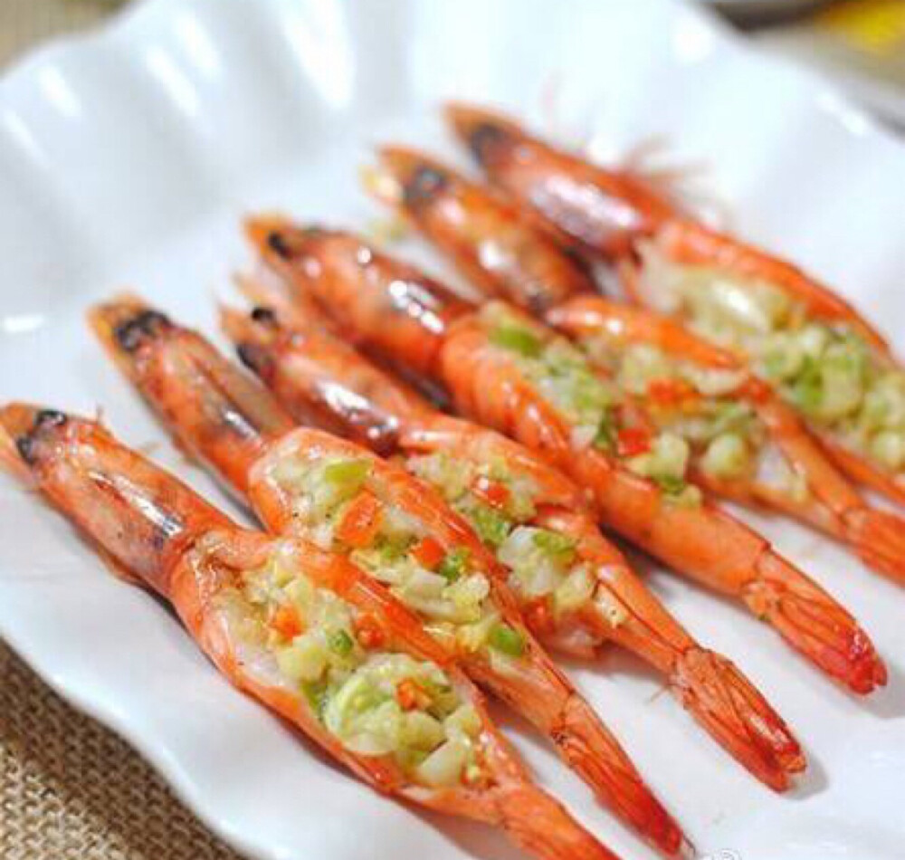 【苹果蒜香烤虾趣】河虾洗净剪去虾枪虾须在虾背上横一刀；挑出虾线淋上料酒、盐腌20分钟；将虾串在竹签上；苹果、蒜瓣、青红椒、葱切成碎末，加盐黑胡椒粉拌匀；微波炉稍微转一会直到黄油融化后拌匀待用；将苹果蒜蓉碎放在片开的虾背上；烤箱预热至180度，放入虾、大蒜，用上下火烘烤10-15分钟即可。