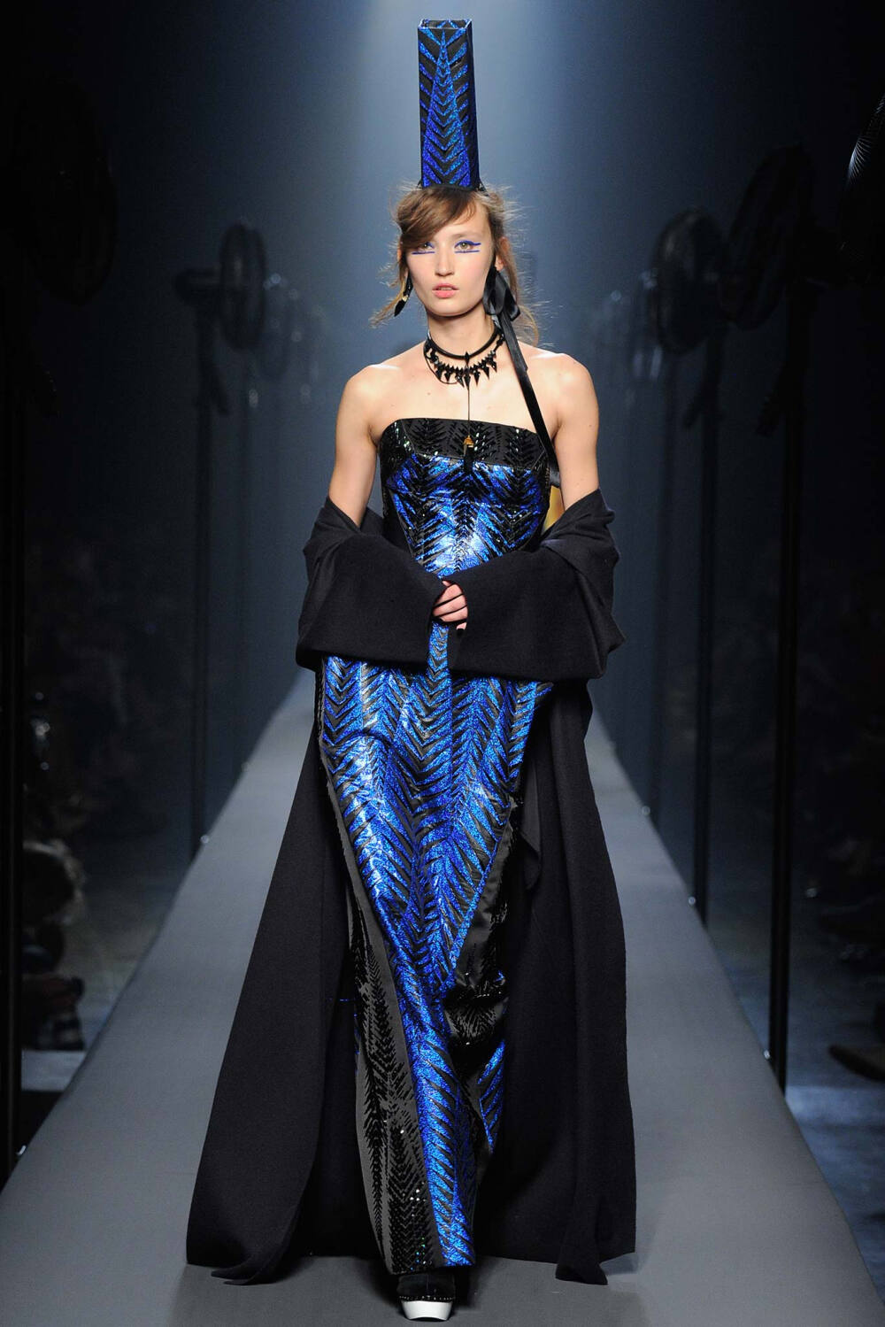 Jean Paul Gaultier Fall 2015 Couture。让·保罗·高缇耶2015秋冬高级定制时装周。本季灵感源于法国布列塔尼 (Brittany) 地区，这里绚烂多姿的民族服饰为高缇耶开启了一场航海旅程?！疤跷啤痹蚴枪岽┦贾铡？〉暮＞跷浦比胫魈?，迸发出畅快呼吸的精神气，而这又不仅仅是一场旅行，更似一局盛大的聚会，狂欢的Party。黑色的主调也不觉单一，多色的火焰式花纹刺绣雕琢着民俗图腾，在裙摆、头饰上绘出历史的传说，极尽奢华，不可小觑的力量从海浪中款款而来。