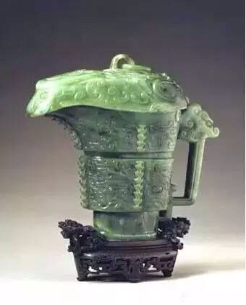 碧玉仿古觥，清乾隆，高18.7cm，口宽7.4cm。 此件碧玉觥是仿古铜器的饕餮纹觥，玉质的墨绿色很自然的呈现着青铜銹斑的色泽，是造办处的精品