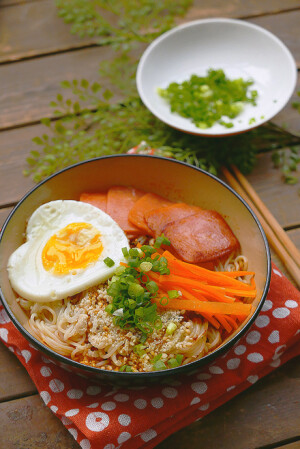 「心形蛋包面」材料：拉面，方火腿肠，鸡蛋，胡萝卜，白芝麻，小葱，盐，味精，水，酱油。
步骤：1.将方肠切好，胡萝切条，葱切末，备用。
2.汤锅里放水，煮沸后下面，待面完全煮散、熟后捞起放入碗内，可以顺道烫一下胡萝卜条。
3.心形煎锅加热后放油，打入鸡蛋，
换小火，放少许糖、盐，盖上锅盖，待双面熟后盛起放入面碗。
4.用煎蛋的余油炒几片方肠，微焦即可。
5.在汤锅里放入适量清水，加葱末、盐、味精、酱油，煮沸后倒入面碗，再撒一把香香的白芝麻，上桌。
tips: 1.推荐使用半干面，口感很棒哒，劲道耐煮，下锅不会糊。
2.我不喜欢黑糊糊的面，如果你也是，可以用生抽，色与味都较浅，或是用白酱油。
3.煎蛋的时候要不时打开锅盖看一下，等里面的蛋熟到你想要的程度时，关火。
4.没有心形煎锅可以用心形模具。
5.依照个人口味可以放蒜泥、醋或辣，喜欢喝汤可以多放些汤水，我主要是怕汤水没了方肠，油散了，味就不美了。
