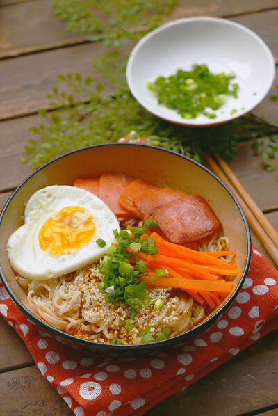 「心形蛋包面」材料：拉面，方火腿肠，鸡蛋，胡萝卜，白芝麻，小葱，盐，味精，水，酱油。
步骤：1.将方肠切好，胡萝切条，葱切末，备用。
2.汤锅里放水，煮沸后下面，待面完全煮散、熟后捞起放入碗内，可以顺道烫一…