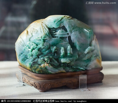 翠雕人物山景山子，高16.1cm，长24.7cm，宽10.5cm。山子翠玉质，带翠玉玉皮颜色。山子上圆雕人物山景。一面利用翠色的深浅表示色泽的不同，采用深雕、凸雕等技法琢出山景，山间有溪流、松树、石阶路和亭台。两老人立…