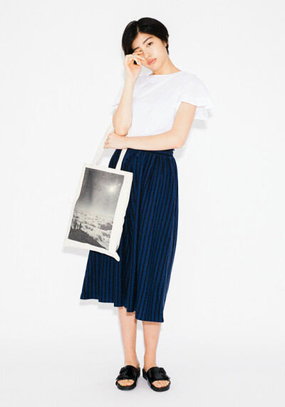 A white design top is combined with a striped skirt. A tote bag printed with a whimsical picture accentuates as a stylish sparkle.