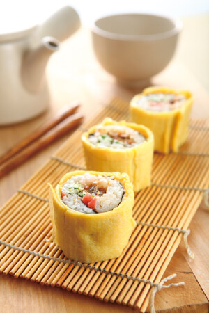 鰻魚蛋捲壽司
材料：
A
醋飯                          適量
市售蒲燒鰻魚            1/2條
市售紅色壽司薑片     適量
小黃瓜    1/2條
白芝麻    少許
海苔片    1片
B
全蛋        2顆
蛋黃        1顆
調味料：
醬油        1/2大匙
味醂        1大匙
米酒        1大匙
作法：
1.將蒲燒鰻魚放入烤箱中略烤，切成長條；小黃瓜切成細絲備用。
2.取海苔片鋪平，在1/2處鋪上適量醋飯、紅色壽司薑片、作法1的材料和白芝麻，捲起備用。
3.將材料B的蛋打入碗中，加入調味料所有材料混拌均勻，取平底不沾鍋加油燒熱，倒入適量蛋液，煎成兩張蛋皮取出備用。
4.在作法2的壽司外，捲上作法3的蛋皮，再適當切段即可擺盤上桌。