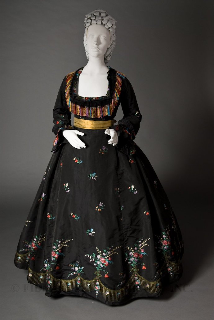 1866，米国新奥尔良，设计者是法国移民服装师Madame Olympe。黑色塔夫绸克里诺林裙，点缀着闪亮的彩色鲜花图案刺绣，领口与袖口上垂下五彩流苏，缎带腰带。抛开总体款式不说，这裙子的细节设计非常奇妙，很有现代感