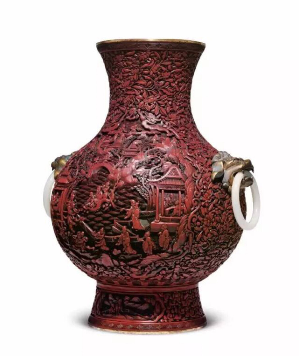 清 乾隆 剔紅百花錦地開光賀壽圖環耳尊，W30 H38cm，此拍品圓形敞口，束頸鼓腹，高圈足。器形周正飽滿，穩重大氣，通體於銅胎上施朱漆，兩側各有一銅鎏金獸頭，口銜白玉環，盡顯凜凜威風，亦帶富貴之氣。器內髹黑漆，漆質渾厚濃郁。口沿及足沿乃至足內皆為銅鎏金做工，足內有“大清乾隆年製”之篆書體款。該器通體的剔紅圖案大致可以分成三個部分。口沿下方與足沿上方各有一圈祥雲紋，將環耳尊之整體環繞其中，彰顯吉祥安定之意。開光外側為百花卷草紋，作為襯托主題的背景卻也絕不單調，卷草紋所特有的韻律感躍動感令其與主題圖案相得益彰而毫不遜色。尊體前後兩側各有一壽桃形開光，其中便是此器的賀壽主題：只見中央有一池，池中碧