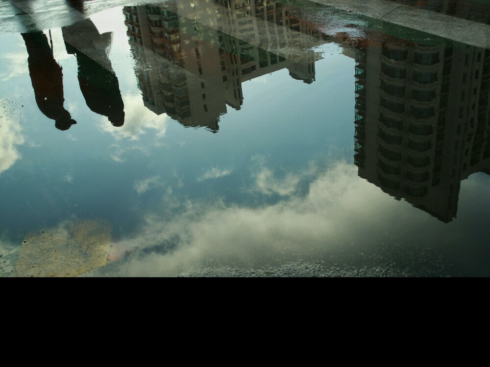 秋雨过后的十字路口积了水，我喜欢拍倒影，也喜欢这张两个人的倒影和高楼的对比感觉。