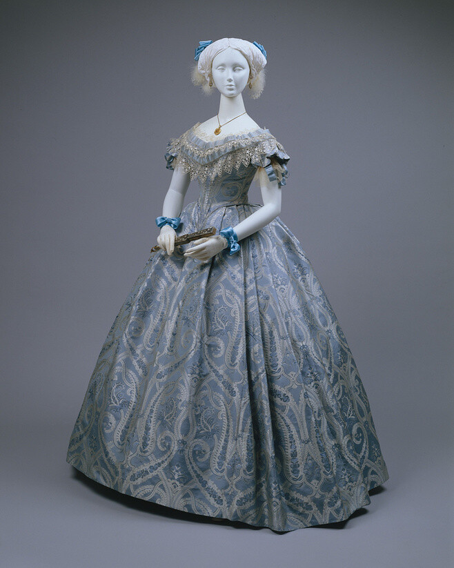 舞裙（1860）。1852年，拿破仑三世即位，在皇后欧仁妮的引领下，女装重拾对洛可可时期繁华的追求，这一时期被成为新洛可可时期，多变的色彩，华丽的面料，以corset紧束的上身和使用crinoline式裙撑的蓬松裙摆，均为这个时期的特点，可以说，是对洛可可时期服装的简洁化。