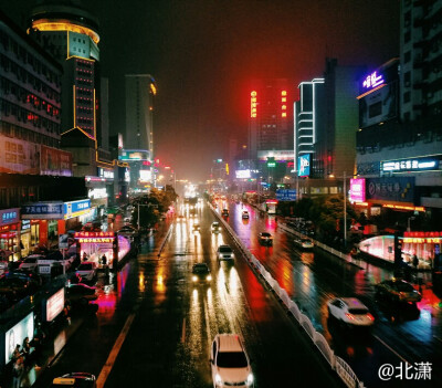商贸雨夜的夜景，灯光璀璨，车辆川流不息。站在天桥上，总有种苍凉的感觉。
