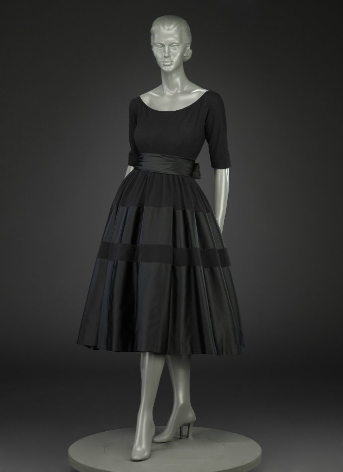  日装，1950s，美国设计大师Norman Norell作品，藏于印第安纳波利斯艺术博物馆。黑色精纺羊毛与丝绸相间的坦领五分袖上衣与大摆裙，这件衣服虽然也是典型的五十年代流行款，但设计上更偏向日常化。