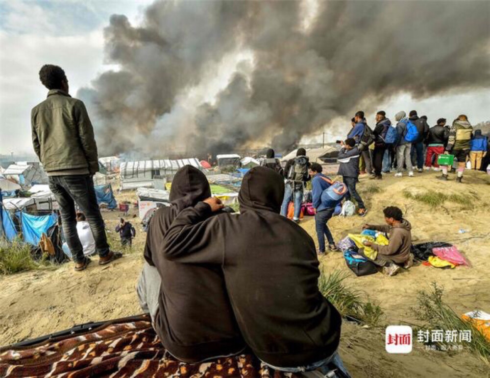 【中东难民潮】2016年10月26日，法国加莱，移民看着浓烟从“丛林”移民营地升起。法国警方持续拆除欧洲这处最大的移民营地，这里聚集着6000-8000人，包括约1300名儿童。
