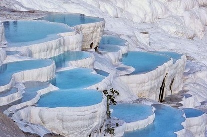 土耳其棉花堡
在土耳其的纺织工业重镇Denizli，位于西南部山区，距离伊兹密尔约二百公里。土文pamukkale是由Pamuk（棉花）和Kale（城堡）两个字组成的，棉花是指其色白如棉，远看像棉花团,其实是坚硬的石灰岩地形。
城堡是说它由整个山坡构成，一层又一层，形状像城堡，故得名棉花堡。
此地多温泉，温泉自洞顶流下，将山坡冲刷成阶梯状，平台处泉水蓄而成塘，人们可坐在里面泡温泉。泉水中的矿物质沉淀下来，把整个山坡染成白色，像露天溶岩。从上往下看，一方方温泉平台像一面面镜子，映照着蓝天白云；从下往上看，像刚爆发完的火山，白色的岩浆覆盖了整个山坡，颇为壮观。棉花堡的形成，正是由于地下温泉水不断从地底涌出，其中含有丰富的矿物质。