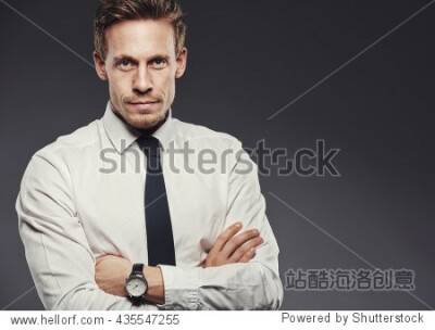 Handsome young businessman in a shirt and tie looking focused, standing with arms crossed against a gray background