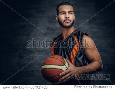 Studio portrait of Black basketball player holds a ball over grey background.