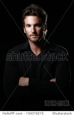 Portrait of determined goodlooking man wearing black shirt, black background.