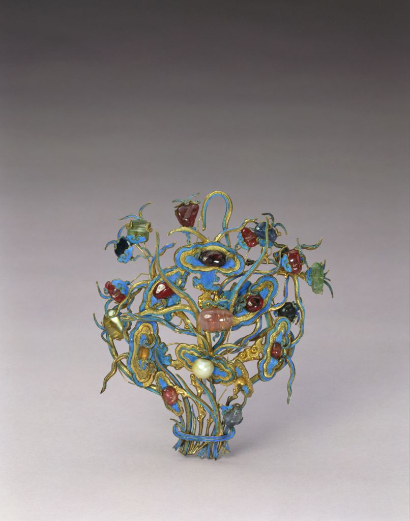 【银镀金嵌珠宝钿花】
清，长14.5cm，宽11.8cm。
钿花银镀金地上雕如意头形灵芝等仙草，仙草纹样用金属线勾勒，曲折四蔓，细腻精工。线条间凹陷处点翠，装饰精美。錾刻加累丝的六朵灵芝内多嵌有宝石，中心一朵所嵌为珍珠。枝叶果实装饰四周，果实以红宝石、蓝宝石、珍珠和晶石等构成。造型生动，纹饰寓意吉祥长寿。